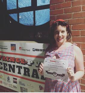 Picture of Maggie, wearing a gingham dress, holding a certificate and smiling.